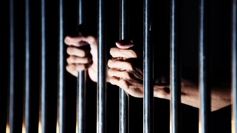 An image of a prisoners hands on the bars of a jail cell.