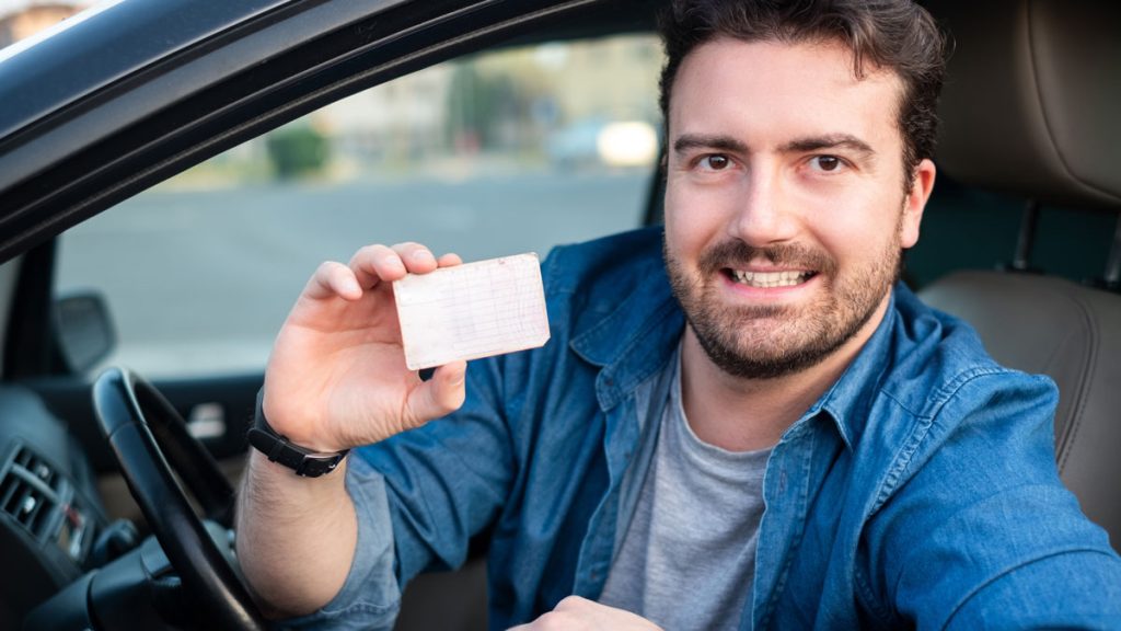 A guy in a car holding up a generic license
