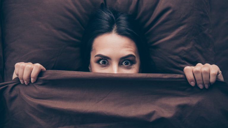 A girl hiding under the covers feeling terrified