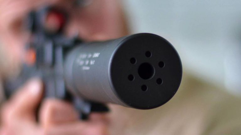 A person aiming a rifle with a suppressor on it