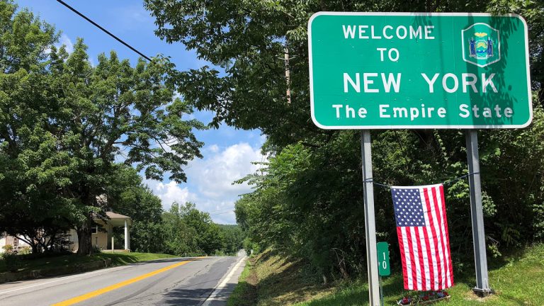 A sign that says 'Welcome to New York' with an American flag hanging underneath it