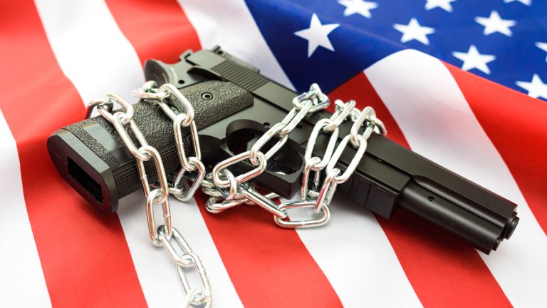 A handgun laying on top of an American flag with chains around it