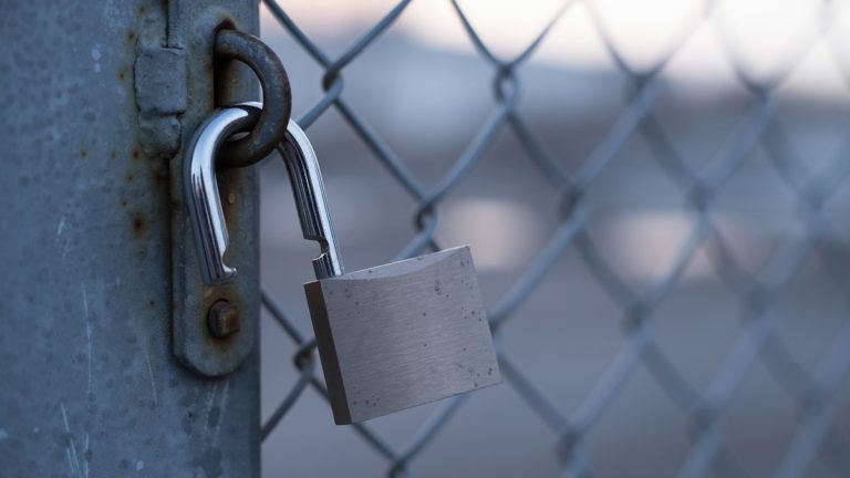 An open padlock hanging on a fence